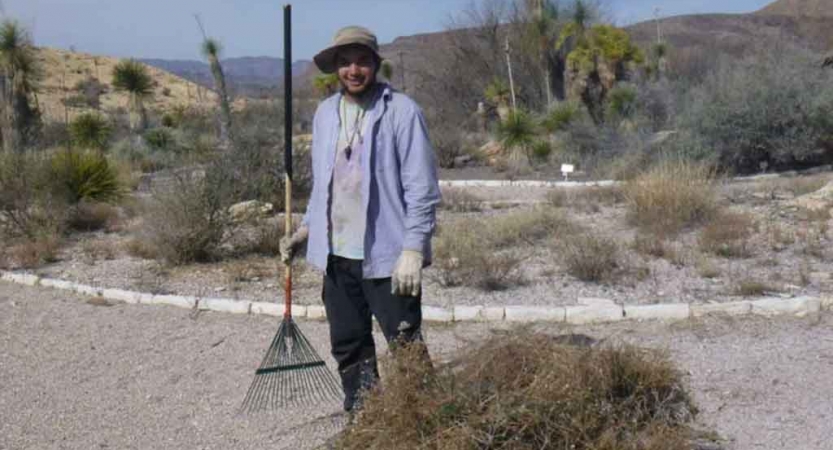 a student holds a rake and stands beside a pile of brush while participating in a service project with outward bound